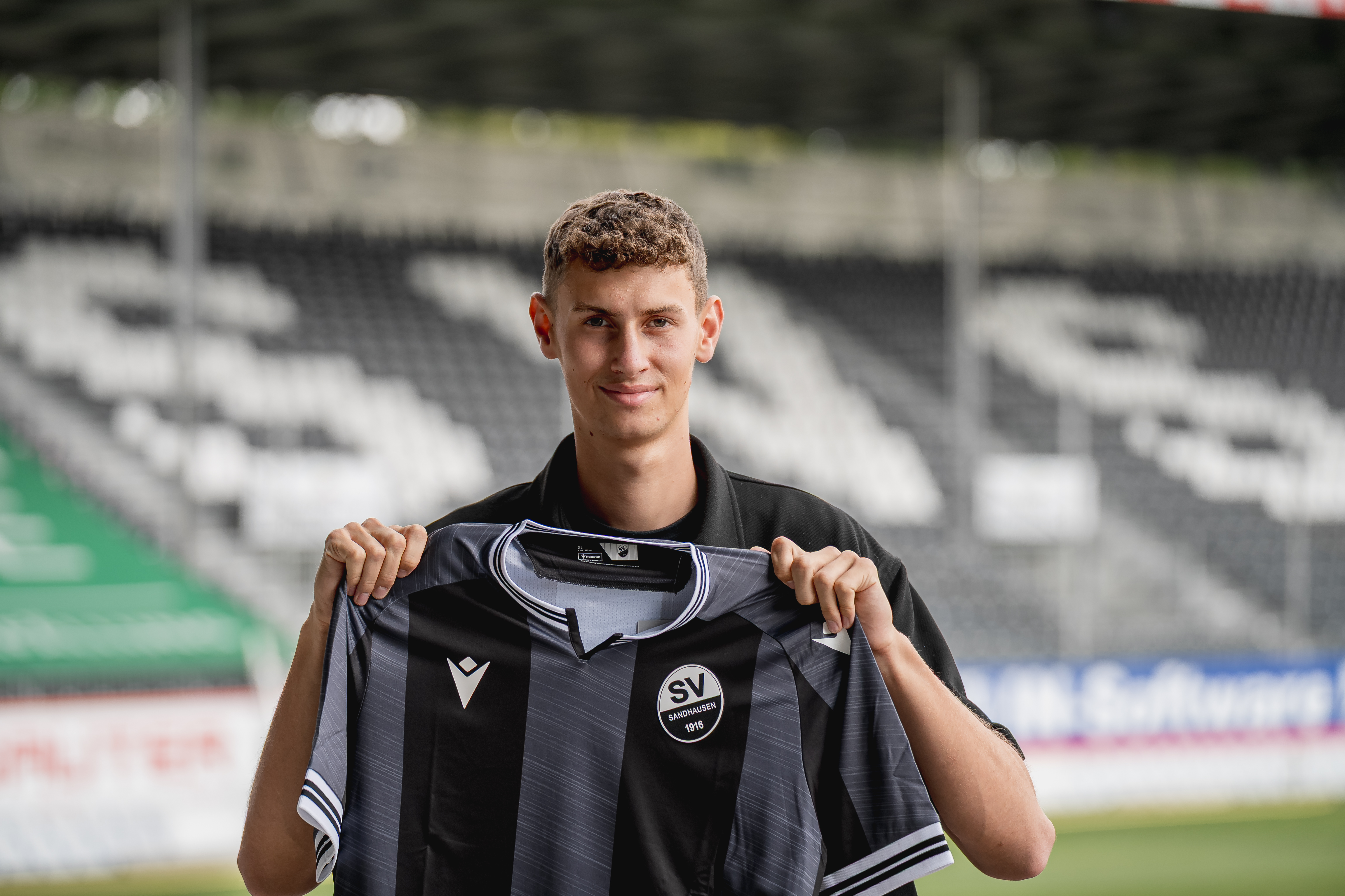 Benedikt Wimmer steht im Stadion und hält das Auswärtstrikot der Saison 2025/26 vor der Brust 